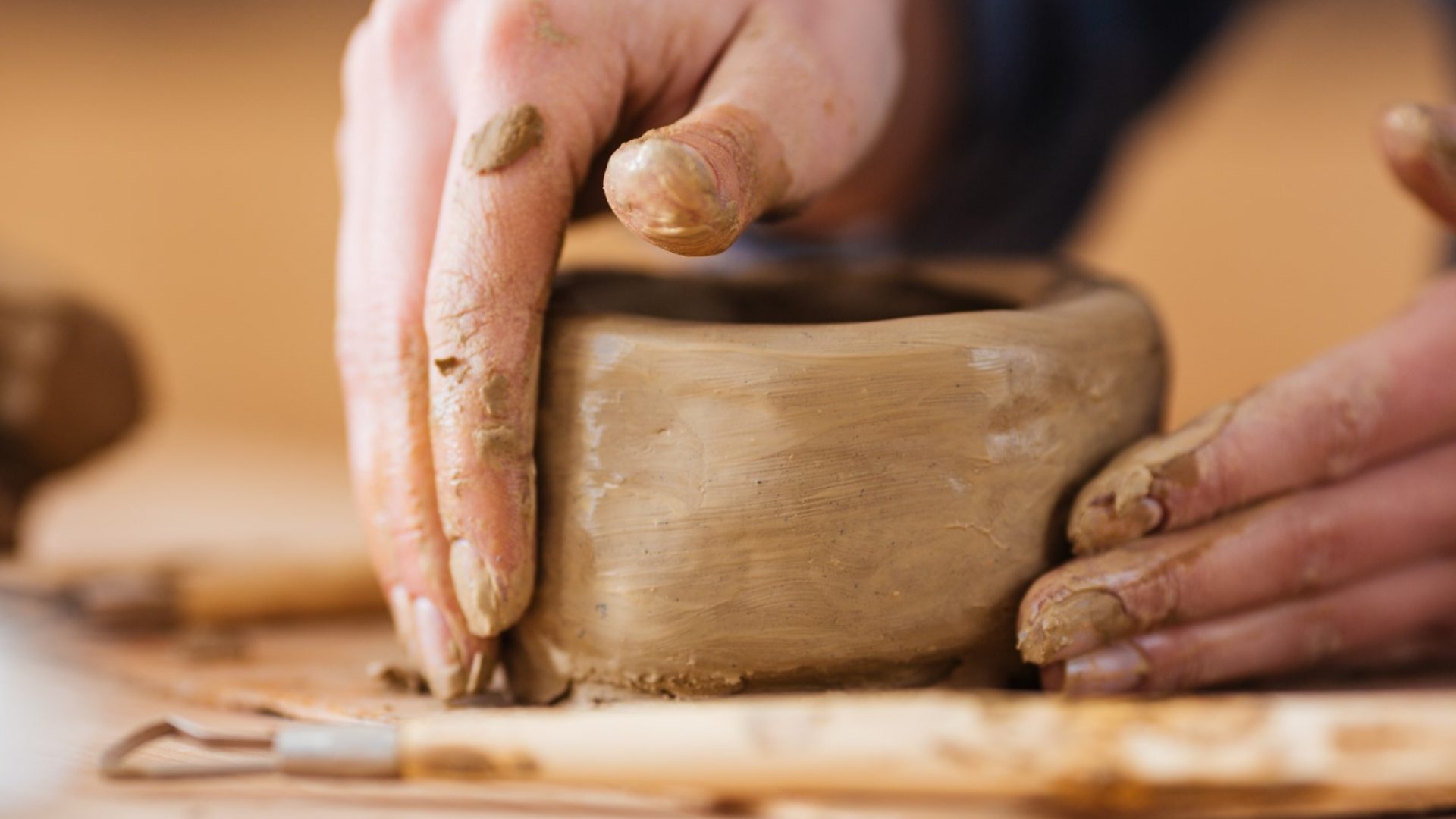 Closeup of earthen jar making by hands of young woman potter in