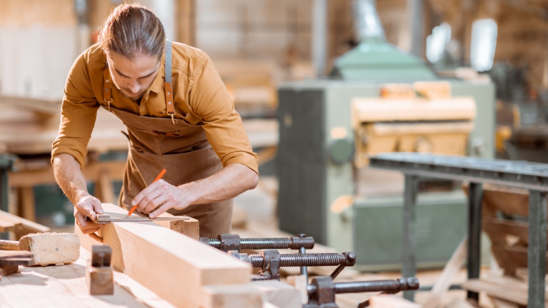 Handsome carpenter working with a wood, marking plank with a pencil in the carpentry workshop